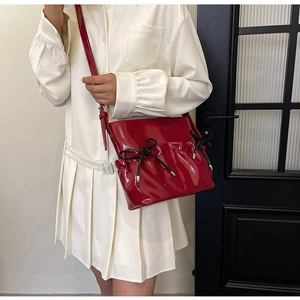 Detail of red faux leather crossbody bag with pleated design and black bow accents