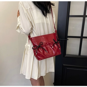 Close-up of red patent leather shoulder bag with decorative bows and ruffled design