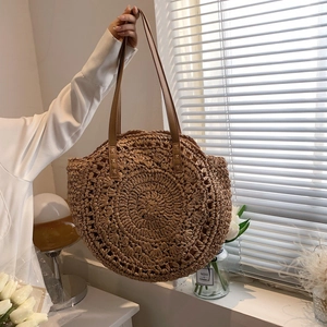 Minimalist round straw tote bag with brown leather straps for beach and vacation style