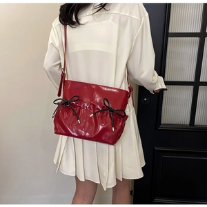 Detail of red glossy PU leather shoulder bag with chic black bows and pleated texture