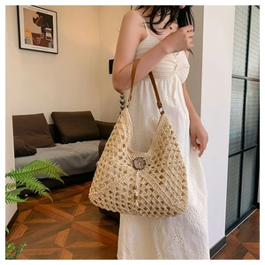 Detail of beige straw hobo bag with woven texture, leather strap and wooden flower charm