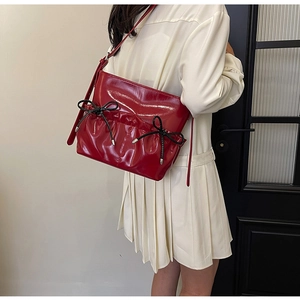 Detail of red glossy PU shoulder bag featuring pleated texture and black bows
