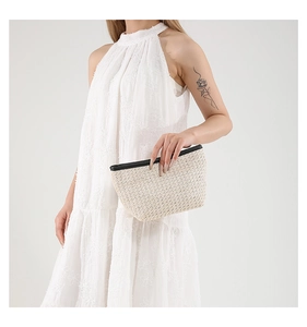 Close-up of a woven straw clutch bag with black PU leather trim held by a model