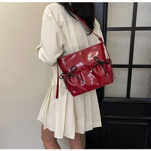 Detail view of red patent leather shoulder bag featuring black bows and pleated design