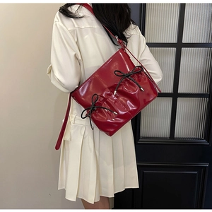 Red glossy faux leather crossbody bag with black bow details worn by a model in a dress