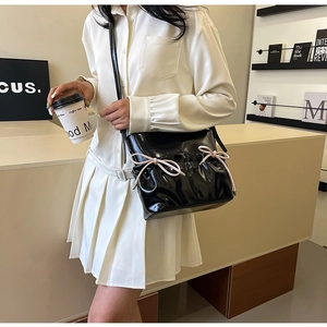 Detail of black patent leather crossbody bag with pink ribbon bows and pleated design