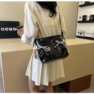 Detail of black glossy PU leather crossbody bag with pink bow accents on a stylish model