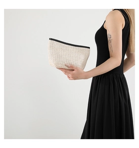 Detail of minimalist woven straw clutch bag with black zipper held by model in hand