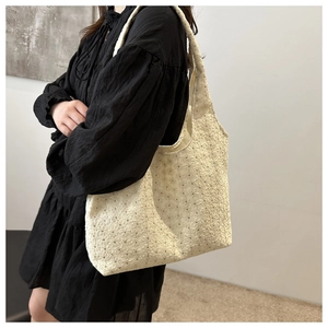 Detail of floral embroidery on beige lace tote bag styled with a black dress