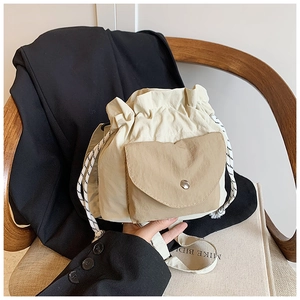 Minimalist cream nylon drawstring bucket bag with tan pocket shown in a lifestyle setting