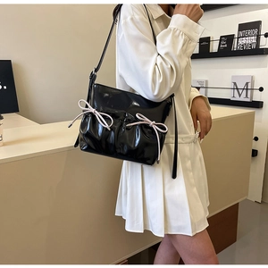 Detail of glossy black PU shoulder bag featuring decorative light pink drawstring bows