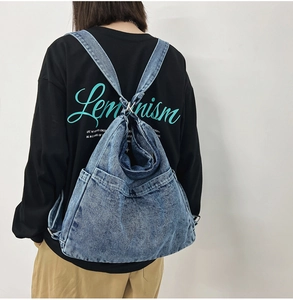 Detail view of washed blue denim backpack with side pockets on female model