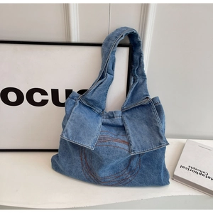 Blue washed denim tote bag featuring circular embroidery and brown strap accents