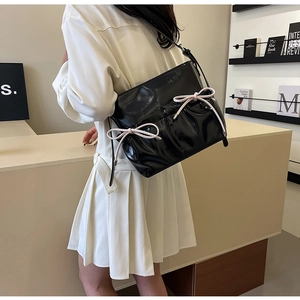 Detail of glossy black patent leather bag with two pink bow accents on the back of model