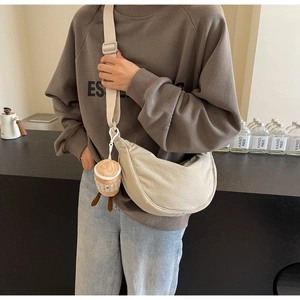 Oatmeal canvas half-moon crossbody bag with wide strap and plush coffee cup charm