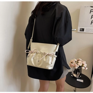 Detail of cream PU leather crossbody bag featuring pink ribbon bows and pleated texture