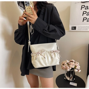 Chic cream white PU leather crossbody bag with pink bows shown on model in modern setting