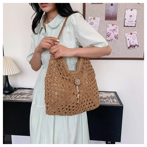 Detail of bohemian straw shoulder bag featuring hollow crochet weave and wood button tassel