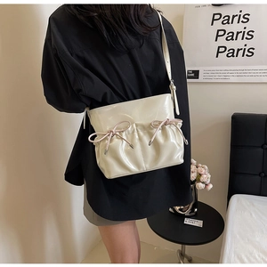 Detail of white patent leather crossbody bag with decorative bow and metal buckle strap