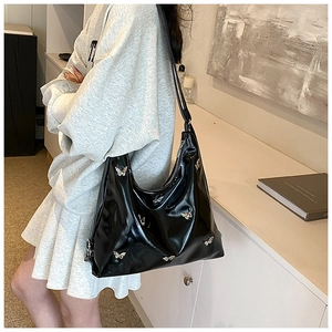 Dettaglio della borsa hobo in vernice nera con farfalle d'argento indossata dal modello