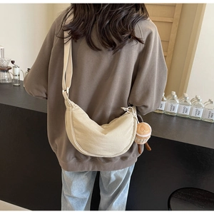 Detail of beige canvas crescent crossbody bag with cute cupcake plush charm outdoors