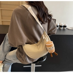 Detail of cream crescent canvas bag with cute coffee plush charm on wide strap