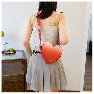 Chic sac à bandoulière rouge en forme de cœur en cuir verni porté par un modèle