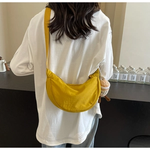 Detail of a bright yellow crescent canvas crossbody bag with adjustable strap and plush charm