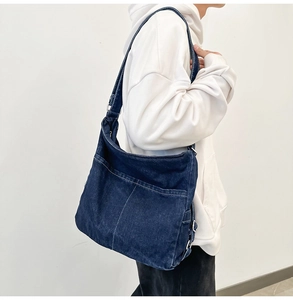 Detail of dark blue denim shoulder bag with white contrast stitching on the front pocket