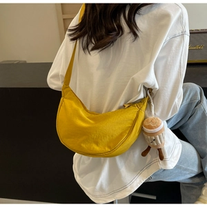 Detail of a bright yellow crescent nylon bag with a brown plush cupcake charm on a shoulder strap