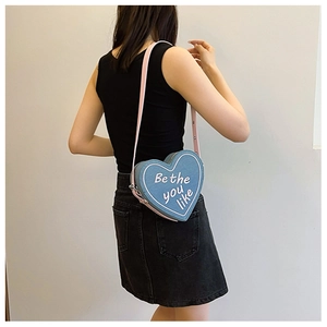 Détail du sac à bandoulière en denim en forme de cœur avec texte blanc sur un modèle