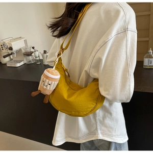 Detail of yellow nylon crescent crossbody bag featuring a smiling coffee cup plush charm