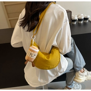 Detail of ginger yellow canvas crescent crossbody bag with cute plush coffee cup charm