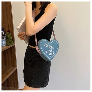 Détail du sac à bandoulière en denim bleu en forme de cœur avec bandoulière rose sur modèle