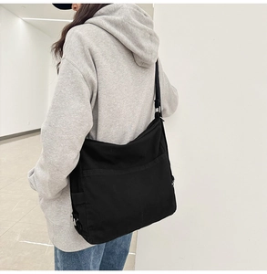 Detail of minimalist black canvas shoulder bag showing reinforced stitching and wide strap