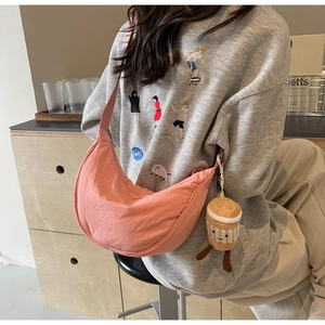 Pink crescent crossbody bag detail with cute coffee cup plush charm on cream background