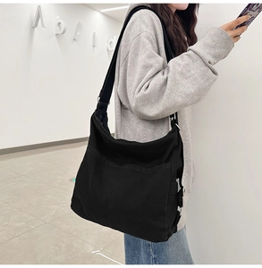 Detail view of the black canvas tote bag showing the adjustable wide strap and metal hardware