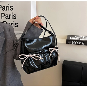 Minimalist black patent leather crossbody bag with pink bow accents and shoulder strap