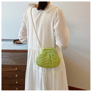 Gros plan du sac en paille vert avec chaîne dorée sur une robe blanche
