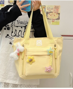 Close-up of yellow nylon tote bag featuring plush star charms and front zip pocket