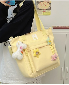 Detail of light yellow nylon tote bag with plush star charms and logo patch on model
