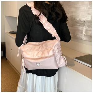 Detail of light pink nylon crossbody bag featuring ruffled strap and bear patch