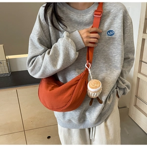 Detail of orange nylon crescent bag featuring a cute coffee cup plush charm and wide strap