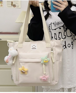 Detailed view of cream nylon tote bag with colorful plush stars and doll pendant