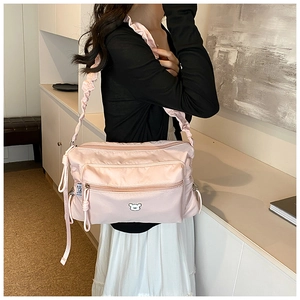 Detail showing the light pink nylon crossbody bag with cute bear patch and ruffled strap