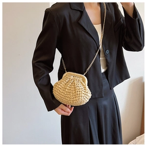 Détail d'un sac en paille tressée beige avec bandoulière chaîne dorée sur tenue noire