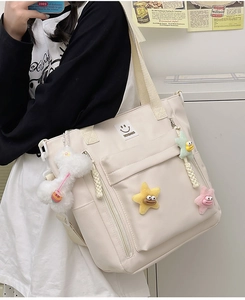 Close-up of cream nylon tote bag with plush charms and brand logo embroidery