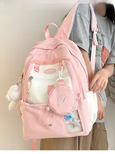 Detail view of pink and white nylon backpack featuring a teddy bear and round coin purse charm