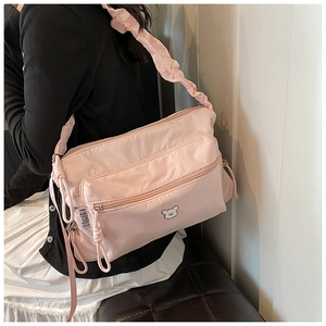 Detail view of pink nylon crossbody bag with ruffled strap and metal bear motif