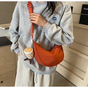 Detail view of burnt orange nylon half-moon crossbody bag with coffee cup charm accessory